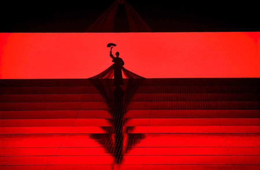 En person står på scen och man ser bara siluetten. En dramatisk bild i bara rött och svart.