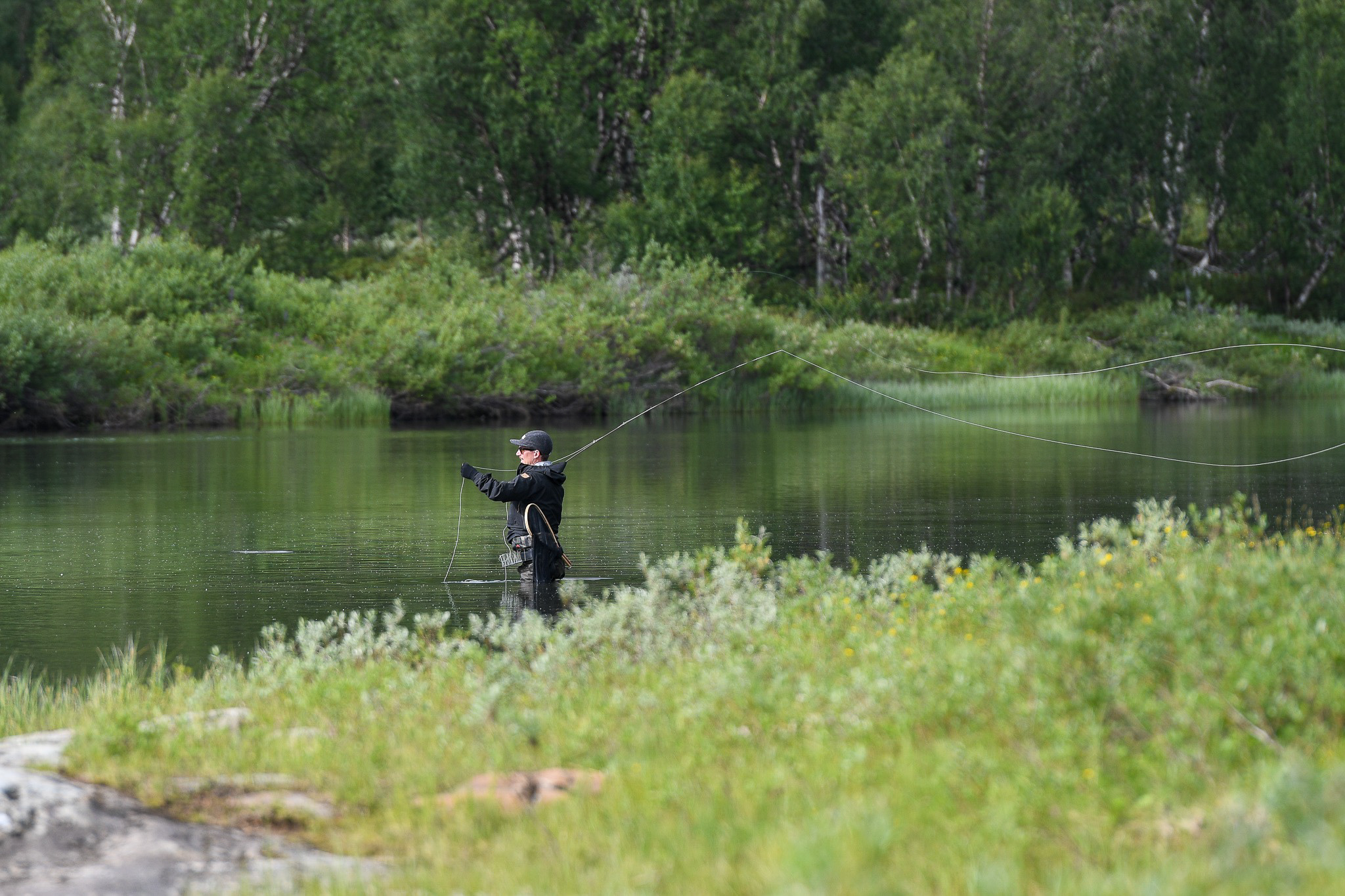 En man står ute i vattnet och fiskar med ett långt smalt flugspö.