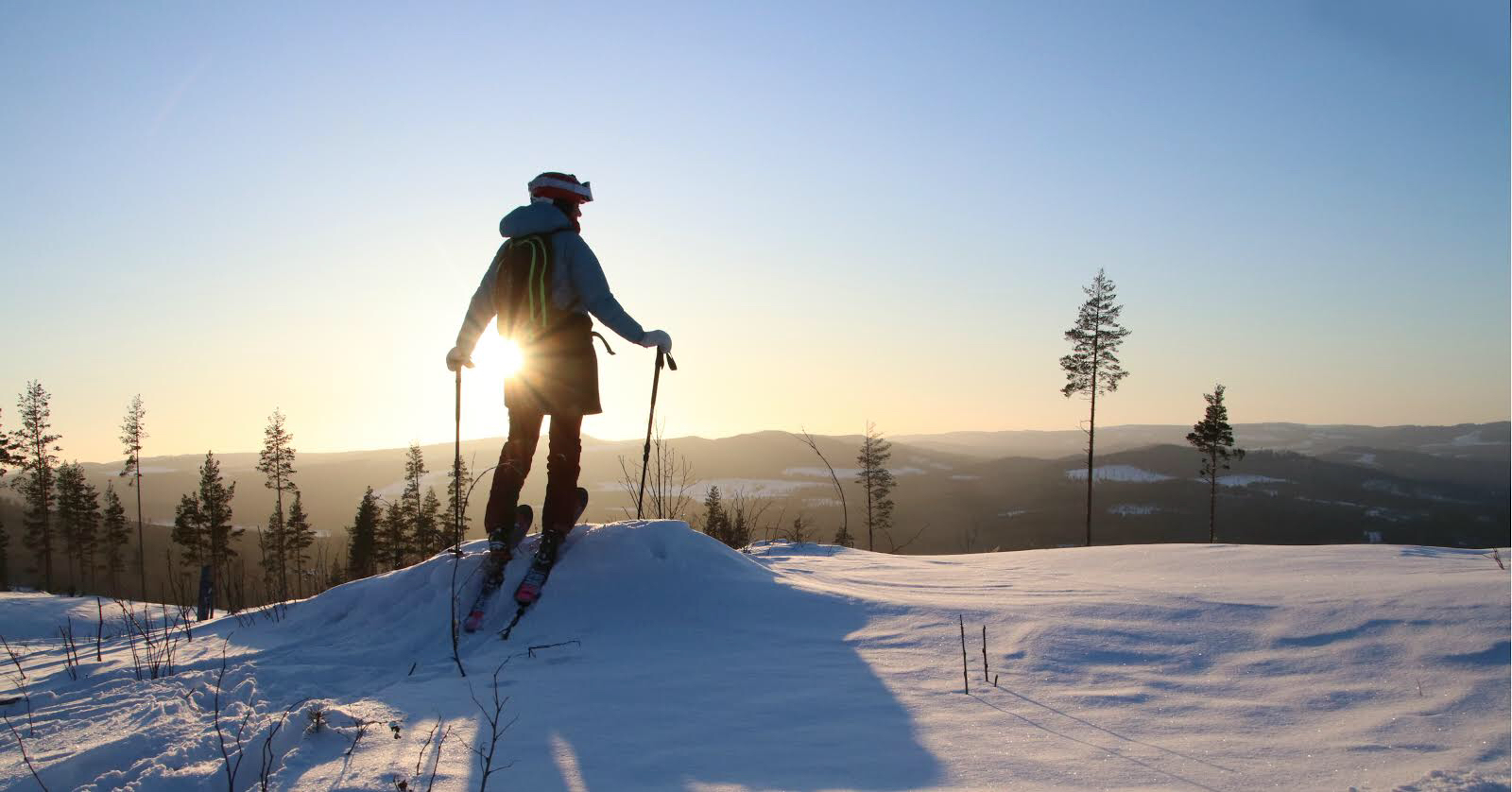 Lotten Rapp ståendes med skidorna på fötterna på ett berg. Solen skiner över det snötäckta landskapet och hon blickar ut över dalen.